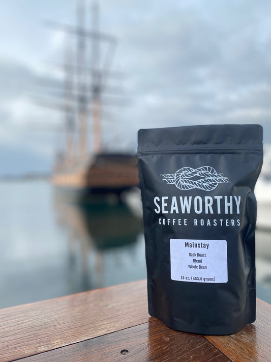 Seaworthy slow roasted, small batch, low acid coffee. 1 pound bag of Mainstay dark roast specialty coffee.  Bag of coffee on Bowens Wharf in Newport Rhode Island.   Old ship with three masts in background.