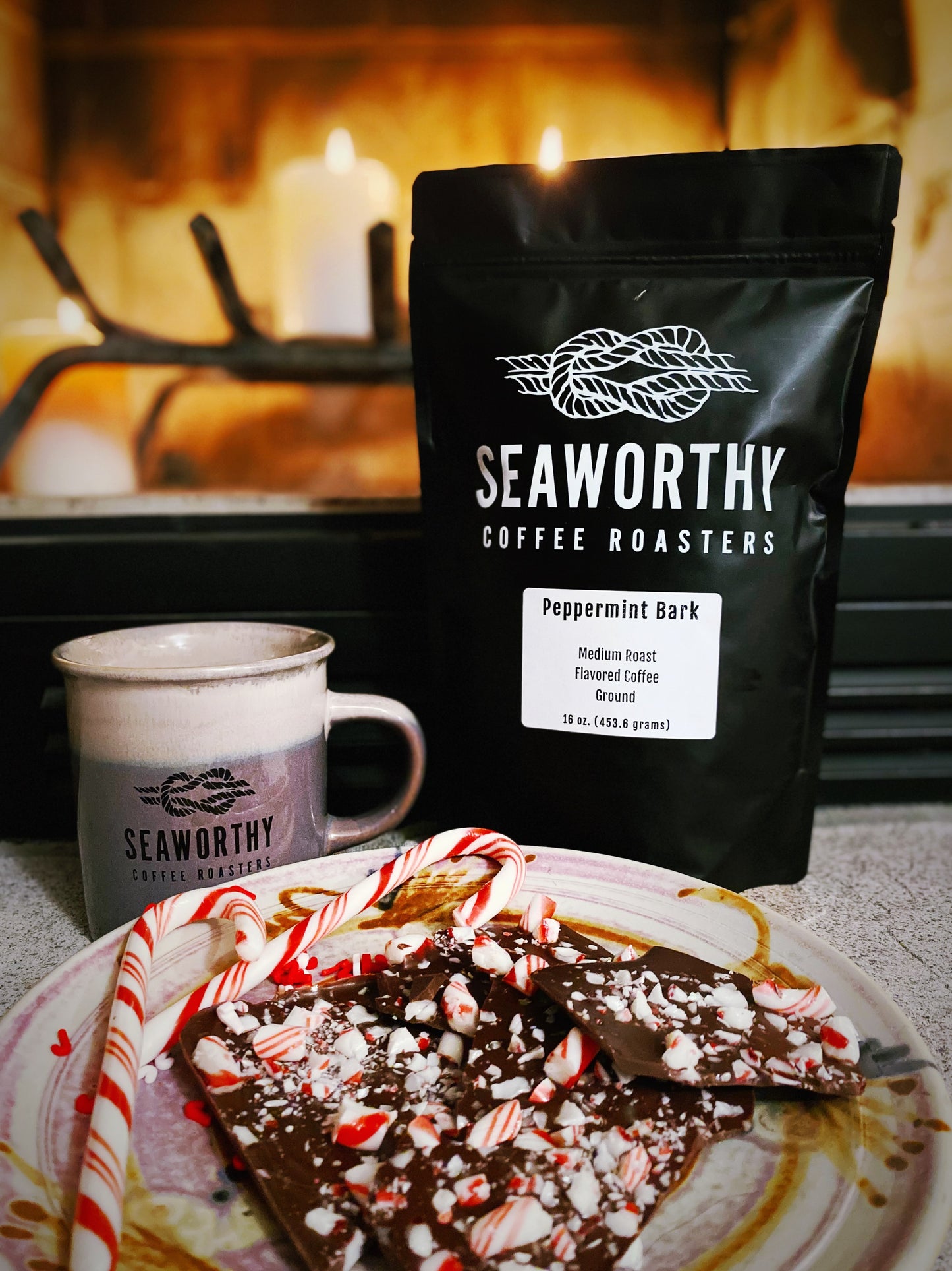 Seaworthy slow roasted, small batch, low acid coffee. 1 pound bag of Peppermint Bark flavored coffee.  Plate of peppermint bark and candy canes.  Warm fire in background.