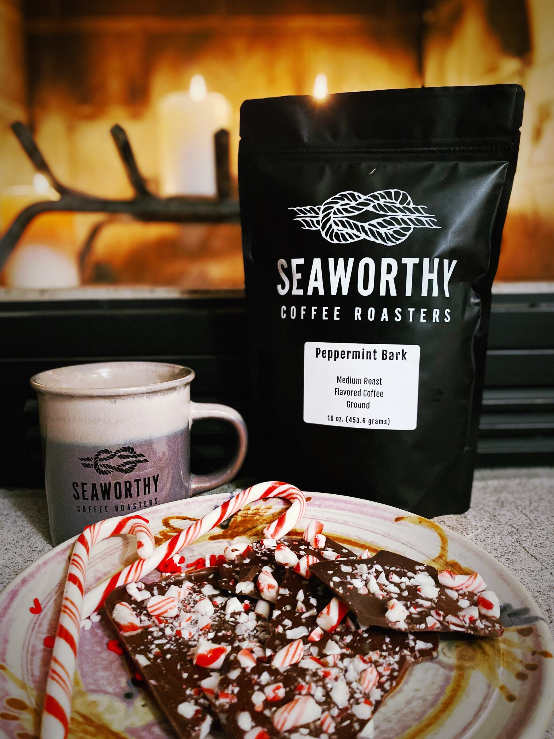 Seaworthy slow roasted, small batch, low acid coffee. 1 pound bag of Peppermint Bark flavored coffee.  Plate of peppermint bark and candy canes.  Warm fire in background.